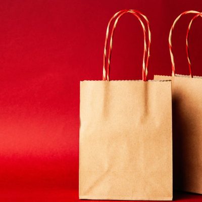 Simple brown paper bags with handle on a festive red backdrop, perfect for Christmas.